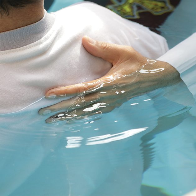 close up of hand on a person's back in a baptism pool