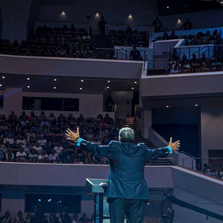 wide shot image from behind Dr. Youssef onstage, extending arms out towards an engaged audience