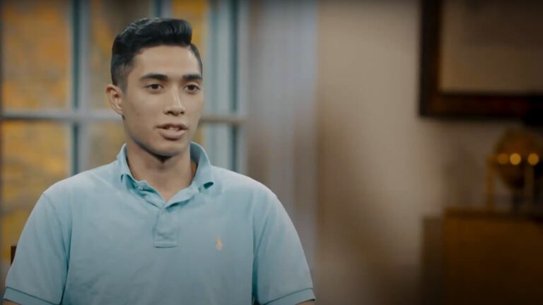 A young man stands in front of a window