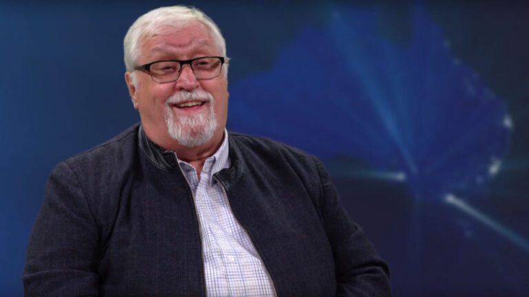A man talks in front of a blue background