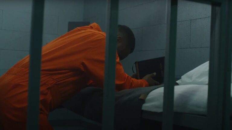 A prisoner in an orange jumpsuit kneels to pray